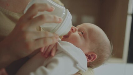 Closeup view of young caucasian mother feeding her baby milk from bottle at home in slow-motion