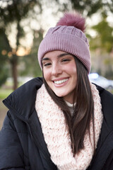 Vertical portrait of beautiful smiling young Caucasian woman with woolen hat looking at camera with positive expression. Happy girl wearing winter clothes Knit and scarf outdoors. Cheerful real people