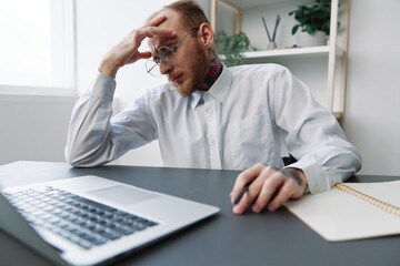 Obraz premium A man in a wheelchair a businessman in the office works, severe fatigue and emotional burnout, integration into society, the concept of work a person with disabilities