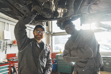 Fototapeta na wymiar Two mechanics wearing uniforms in a car repair shop posing under a car on a lift. High-quality photo