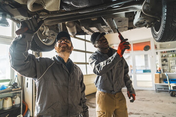 Fototapeta na wymiar Two mechanics working under a lifted car using tools in a modern car repair shop. High-quality photo