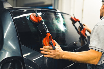 Unrecognisable man instaling rear window pane in the back of car using professional tools. Car...