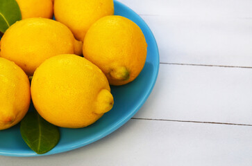 Fresh ripe yellow lemon fruits on a blue plate on a white wooden background.Healthy eating or diet concept with space for text.Selective focus.