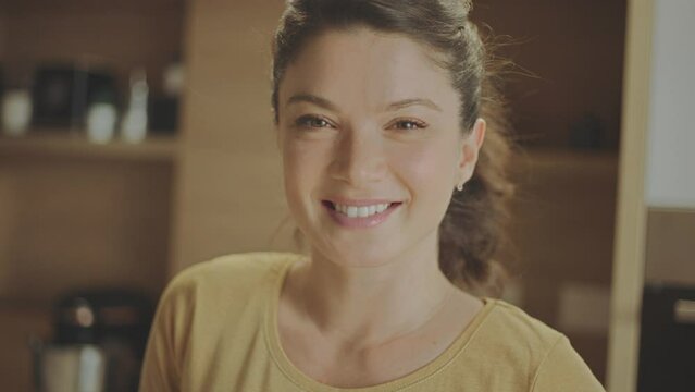 Close-up portrait shot of a young woman looking at camra and smiling while standing in the kitchen. Shot in slow-motion