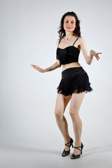 Beautiful young woman with evening make-up and hairdo dancing in elegant black dress with passion. Studio portrait on a gray background. Dancing, tango style.