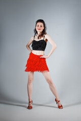 An elegant dancer performs a Latin American dance in an elegant red dress with sparkling jewelry. Fashion and beauty. Ballet show. Studio portrait.