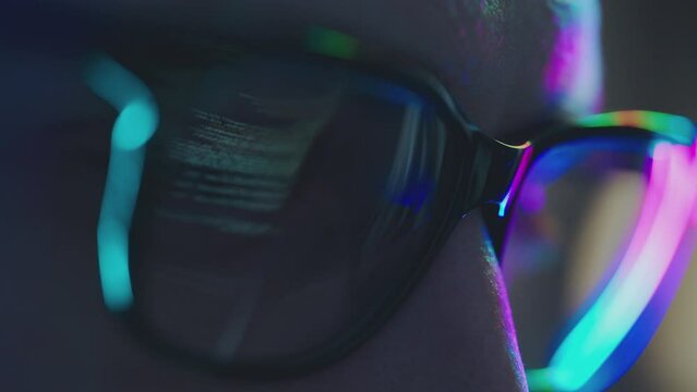 Close-up portrait of software engineer working on computer, line of code reflecting in glasses