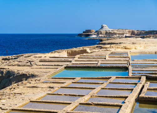 Salt pans on the coast of Gozo, Malta with Xwejni Rock in the background and blue sky