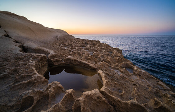 Salt pans on the coast of Gozo, Malta at sunset with orange and purple sky