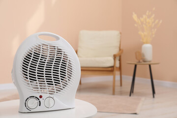 Compact electric fan heater on white table indoors, closeup. Space for text