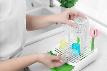Woman putting baby bottles on dryer after sterilization in kitchen, closeup