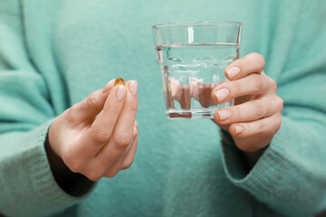 Woman holding glass of water and pill, closeup view