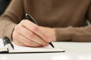 Man writing in notebook at white table, closeup. Space for text