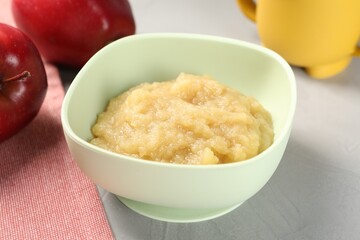 Healthy baby food. Bowl with delicious apple puree on light grey table, closeup