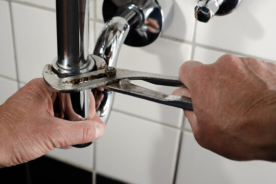 Klempner mit Rohrzange am Abfluss Siphon repariert Sanit&auml;r Wasser Installation Installateur Rohrleitung POV