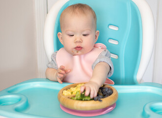 Baby eating broccoli. Baby-led weaning. Weaning. Healthy eating. Caucasian baby girl sitting in a...
