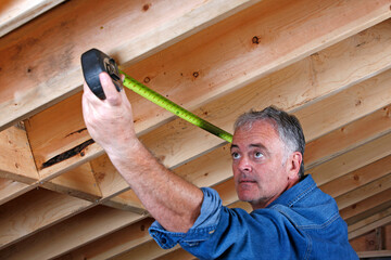 Mature man measuring distance between rafter beams of home addition.