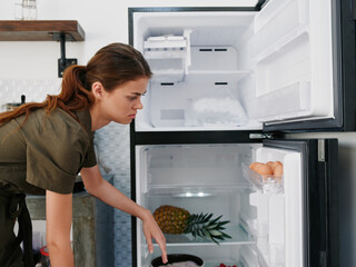 A woman opened the refrigerator and looks sadly into it, wondering what to cook, defrosted the refrigerator, freezer repair in the kitchen at home