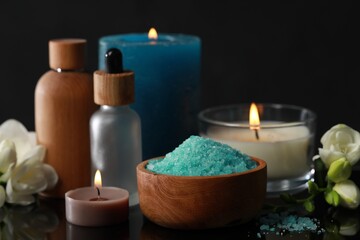 Beautiful spa composition with different care products, burning candles and flowers on black mirror surface, closeup