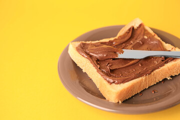 Spreading chocolate paste onto bread on yellow background, space for text