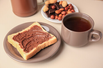 Tasty toast with chocolate paste and cup of tea served on light table