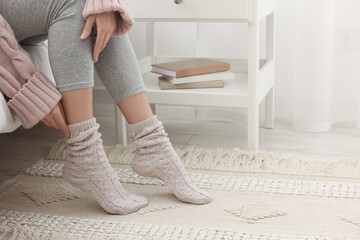 Woman wearing warm knitted socks at home, closeup. Space for text