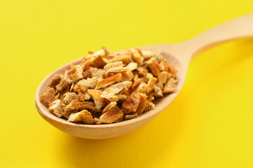 Spoon with dried orange zest seasoning on yellow background, closeup