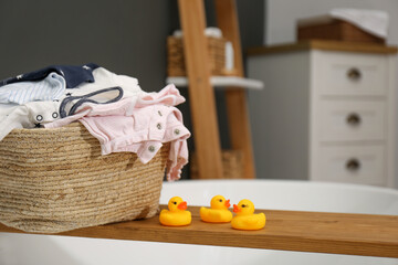 Fototapeta na wymiar Laundry basket with baby clothes on tub tray in bathroom, closeup. Space for text
