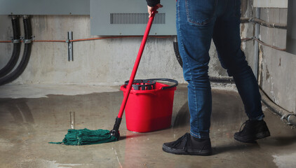 Woman mopping flood from water leaks in basement or electrical room. Water damage from rain,...