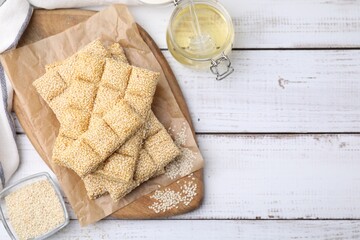 Delicious sweet kozinaki bars, sesame seeds and honey on white wooden table, flat lay. Space for text