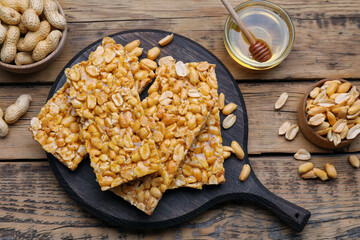 Delicious peanut kozinaki bars, nuts and honey on wooden table, flat lay