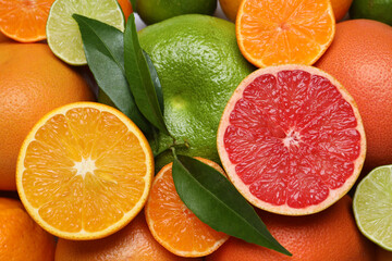 Different citrus fruits with fresh leaves as background, top view
