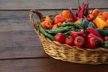 Fototapeta na wymiar Wicker basket with many different fresh chilli peppers on wooden table, space for text