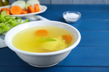 Delicious chicken bouillon with carrot and celery on blue wooden table, closeup