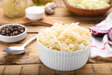 Bowl of tasty sauerkraut and ingredients on wooden table, closeup