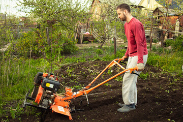Planting vegetables under the walk-behind tractor. A man with a walk-behind tractor in the garden. Manual work with equipment. An elderly man teaches a young boy to plow the land.