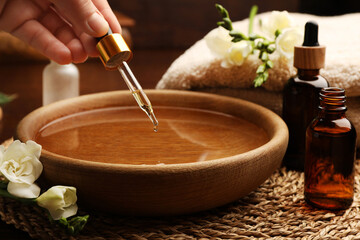 Obraz na płótnie Canvas Woman dripping essential oil into bowl at table, closeup. Aromatherapy treatment