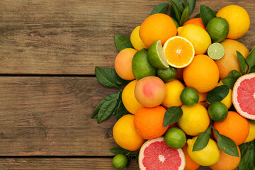 Different citrus fruits with green leaves on wooden table, flat lay. Space for text