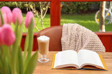 Naklejka na ściany i meble Glass of delicious cocoa, book on wooden table and chair with blanket at terrace