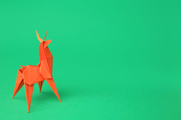 Origami art. Handmade orange paper deer on green background, space for text