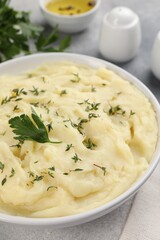 Bowl of tasty mashed potato, parsley, olive oil and pepper on grey marble table, closeup