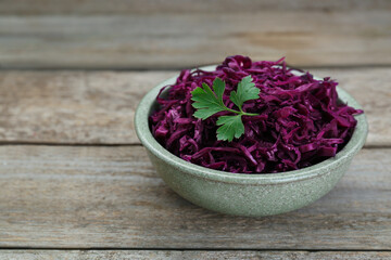 Obraz na płótnie Canvas Tasty red cabbage sauerkraut with parsley on wooden table. Space for text