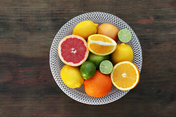 Bowl with different citrus fruits on wooden table, top view