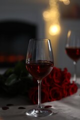 Glasses of red wine and rose flowers on grey table against blurred lights. Romantic atmosphere