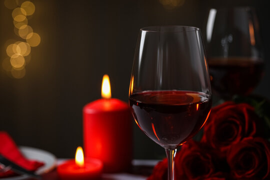 Glasses of red wine, burning candles and rose flowers against blurred lights, space for text. Romantic atmosphere