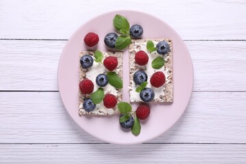 Fototapeta na wymiar Plate with crispbreads, berries and mint on white wooden table, top view