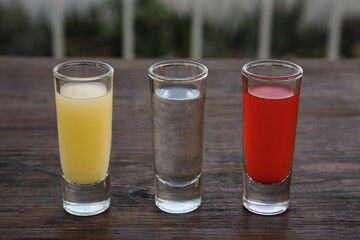 Shots with lime juice, tequila and sangria as colors of mexican flag on wooden table. Traditional serving