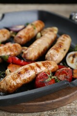 Tasty fresh grilled sausages with vegetables on wooden table, closeup