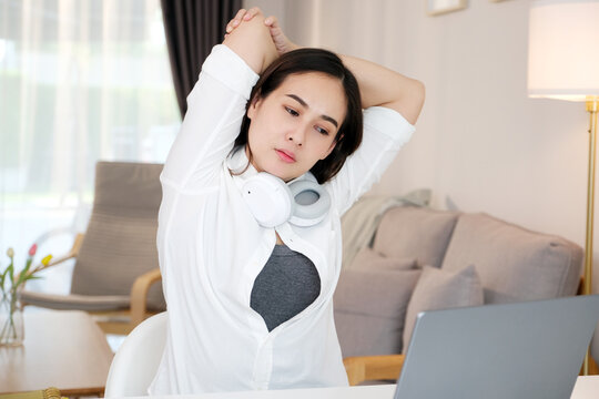 Young asian woman stretching body for relaxing while working with laptop computer at her desk, home office lifestyle