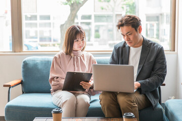 Fototapeta premium カフェでパソコンを使って仕事を教える・話すビジネスマンとビジネスウーマン（アジア人・男女） 